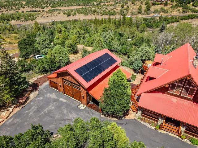 Log cabin exterior featuring a red metal roof, solar panels, and a paved driveway