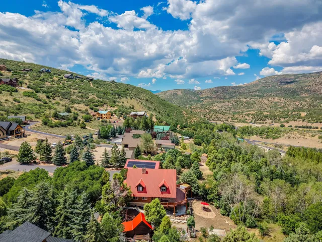 Hillside property featuring a distinctive red roof, solar panels, and extensive surrounding tree cover