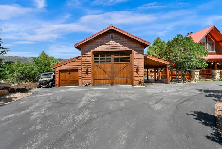Tarmac driveway providing access to a two-car garage with arched wooden doors and an additional single-car garage