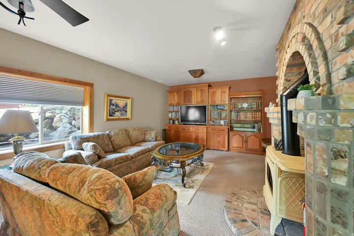 Carpeted living area featuring a brick fireplace with an arched opening, a wood-finish built-in entertainment center, and a window with wood trim