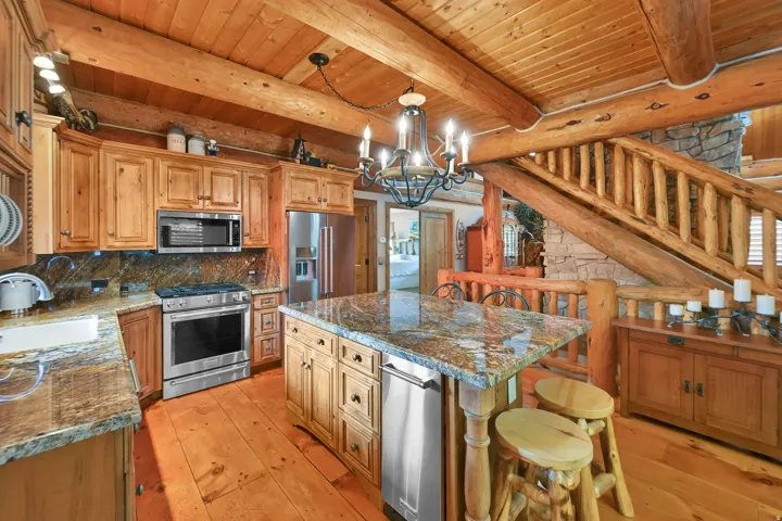 Kitchen featuring custom wood cabinetry, stainless steel appliances, a multi-tone stone countertop island, and wood-finish flooring