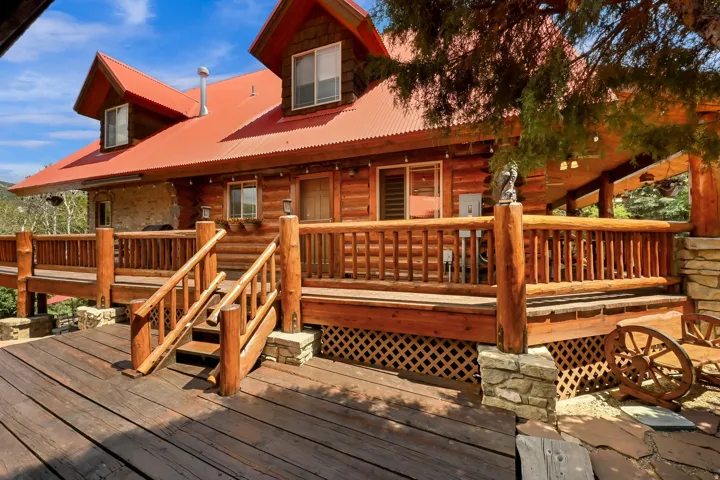Expansive log cabin exterior featuring a red corrugated metal roof, multiple dormer windows, and a generous wrap-around deck