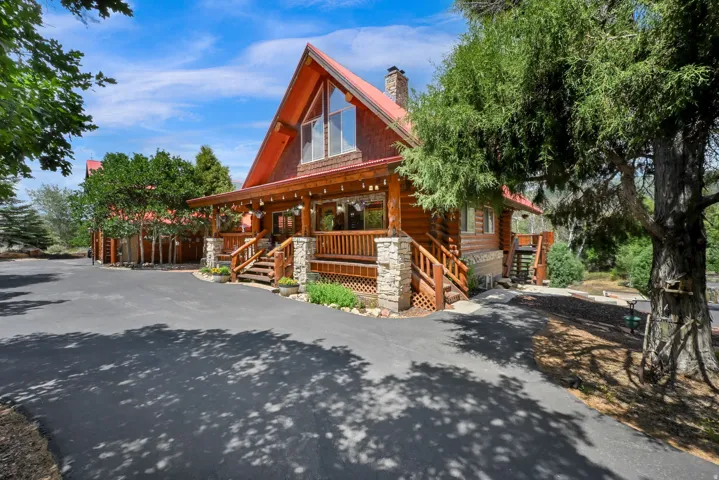 Log cabin exterior featuring a red metal roof, stone chimney, extensive wood decking, and A-frame window design