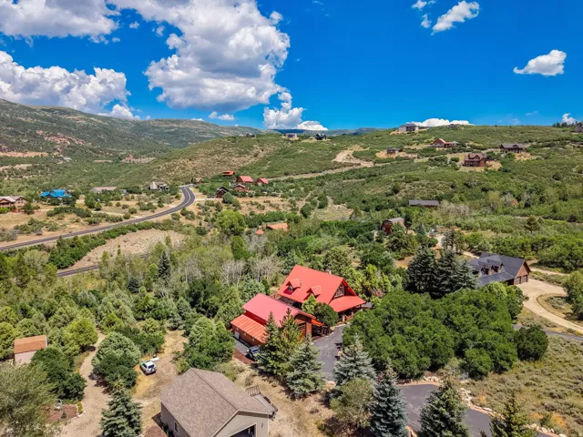 Expansive mountain landscape featuring a large property with a red metal roof and surrounding mature trees