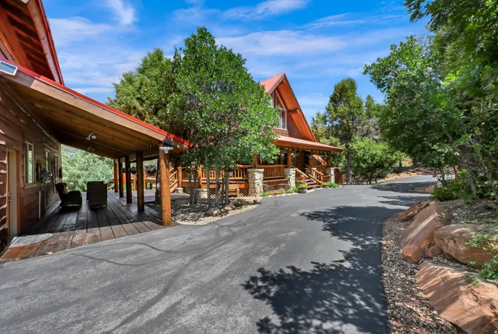 Asphalt driveway winding towards a cabin-style property featuring a covered wood deck, wood siding, and a red metal roof
