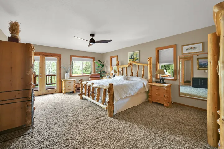 Carpeted bedroom featuring a ceiling fan, dual windows, and French doors opening to an exterior balcony