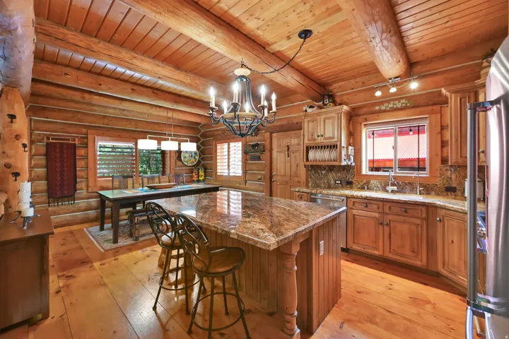 Spacious kitchen featuring exposed wood log walls and ceiling, wood-finish flooring, a central island with a stone-finish countertop, and recessed panel wood cabinetry