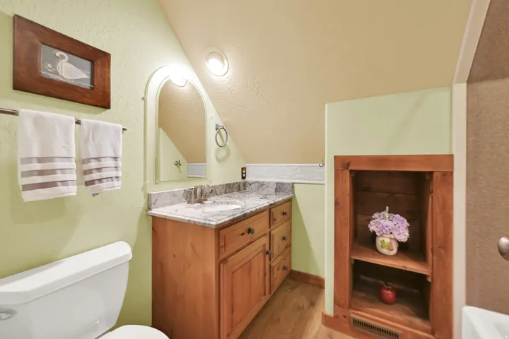 Bathroom featuring a vanity with a light-toned wood finish, a granite-style countertop, and an arched mirror