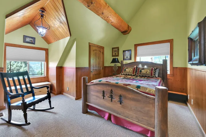 Sloped wood-finish plank ceiling with exposed wood beam and suspended pendant light fixture