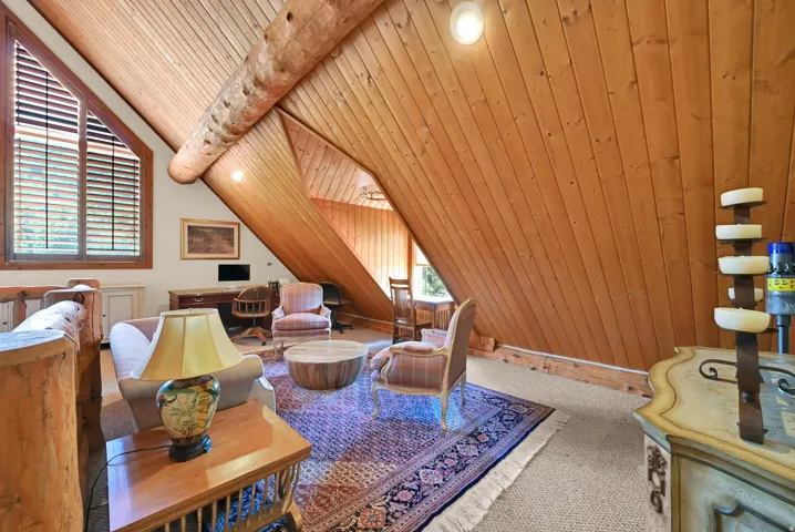 Vaulted wood-paneled ceilings with exposed log beams and a large triangular window featuring horizontal slat blinds