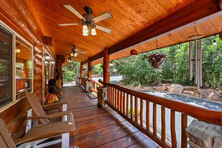 Expansive wood-finish porch featuring a ceiling fan, exposed wood beam ceiling, wood-finish flooring, log-style railing, and stone pillar accents