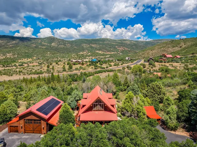 Mountain property featuring a main residence with a red roof, a detached garage with solar panels and wood carriage-style doors, and extensive surrounding greenery