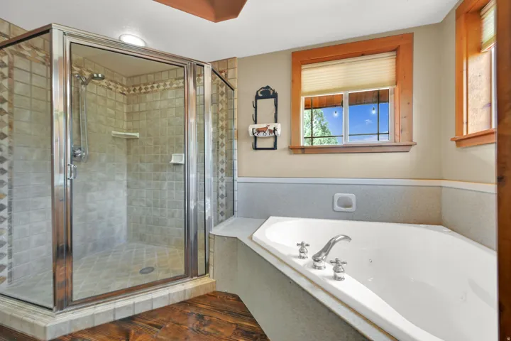Enclosed shower with tiled walls and floor, soaking tub, wood-finish flooring, and natural wood window trim