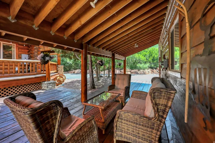 Covered wood deck featuring exposed beam ceiling, wood-plank flooring, and log-cabin exterior