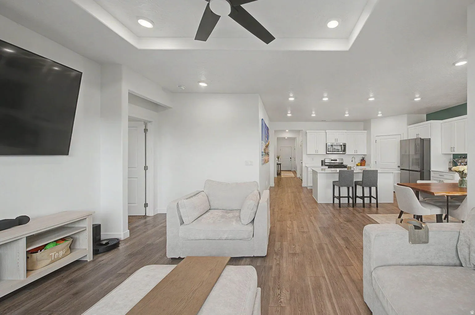 Open-concept living space featuring wood-finish flooring, recessed lighting, and a tray ceiling with a ceiling fan