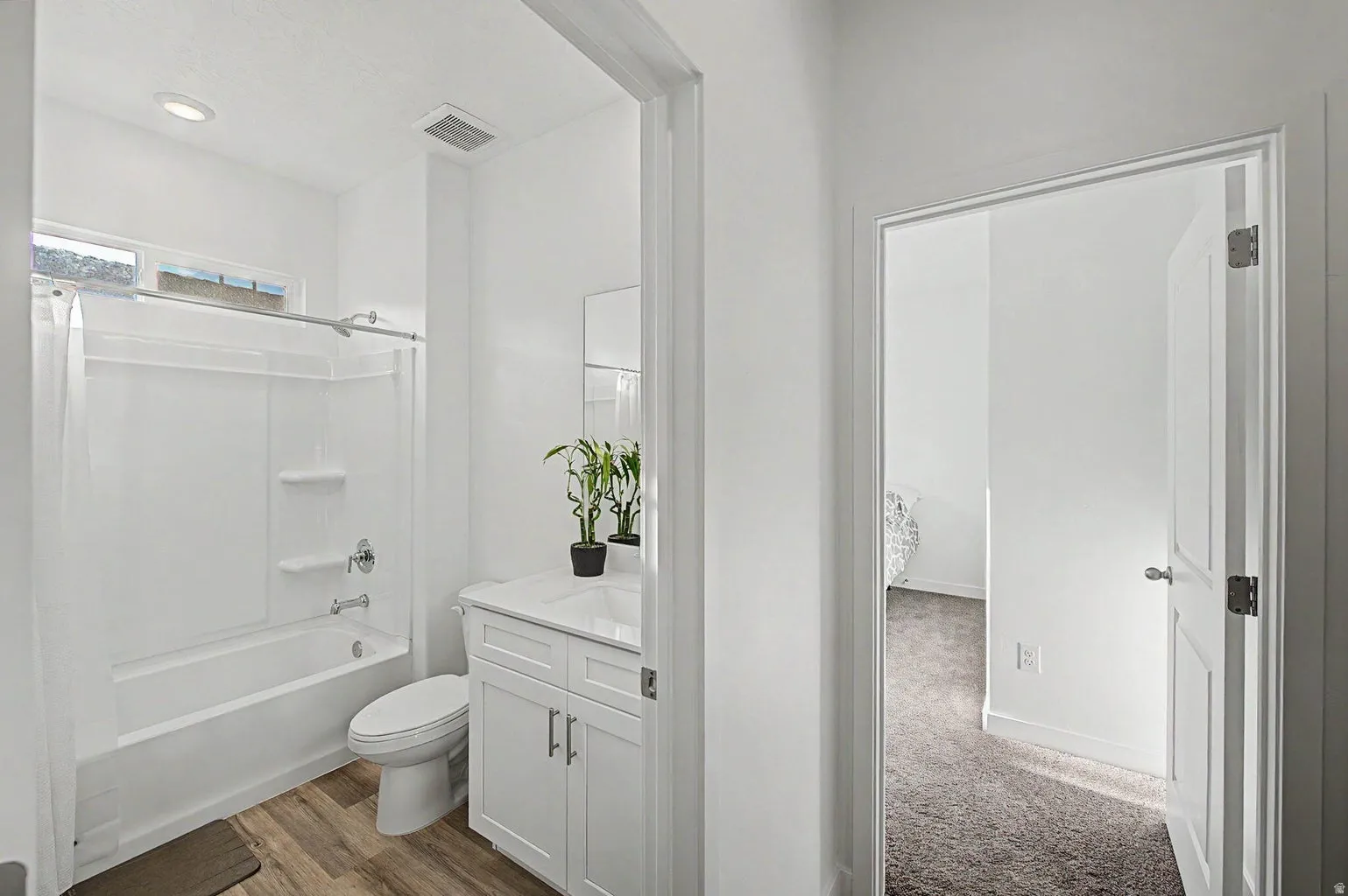 Bathroom featuring a white vanity with a white countertop and integrated sink, a white toilet, and a white tub and shower combination with a single-handle faucet