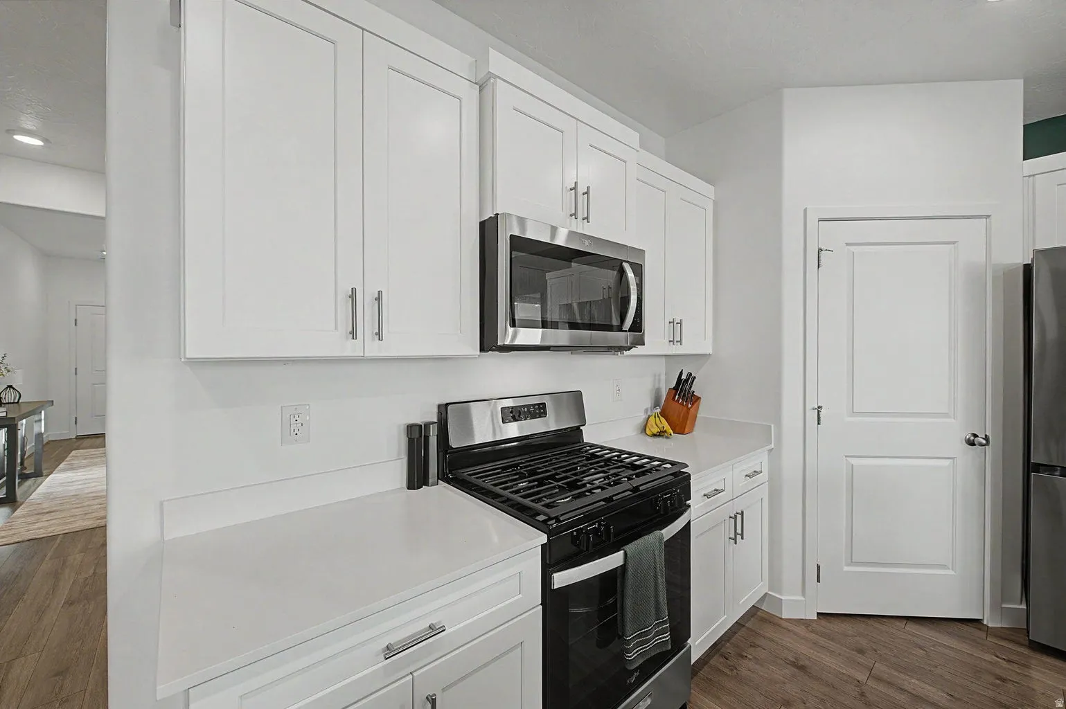 Kitchen featuring white shaker cabinetry, stainless steel appliances, light-toned countertops, and wood-finish flooring