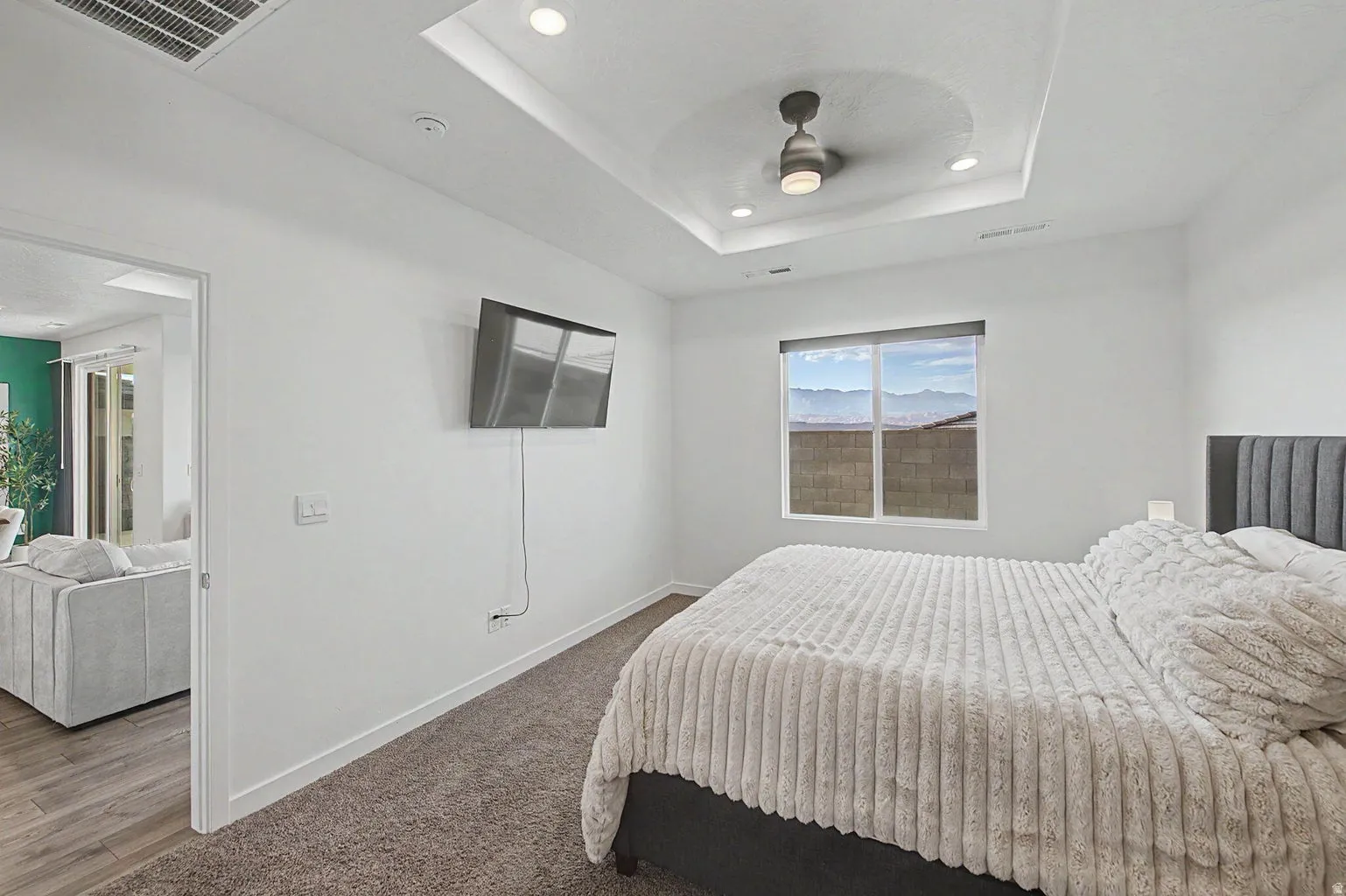 Recessed lighting, a ceiling fan, and a tray ceiling accent this room