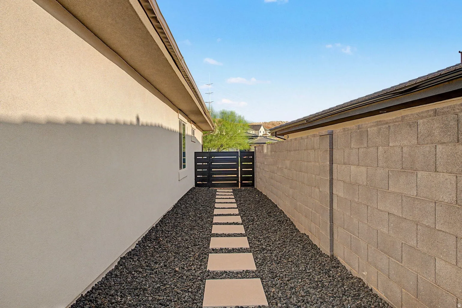 Exterior side yard featuring a stepping stone pathway set in dark gravel, stucco siding, and a block wall perimeter