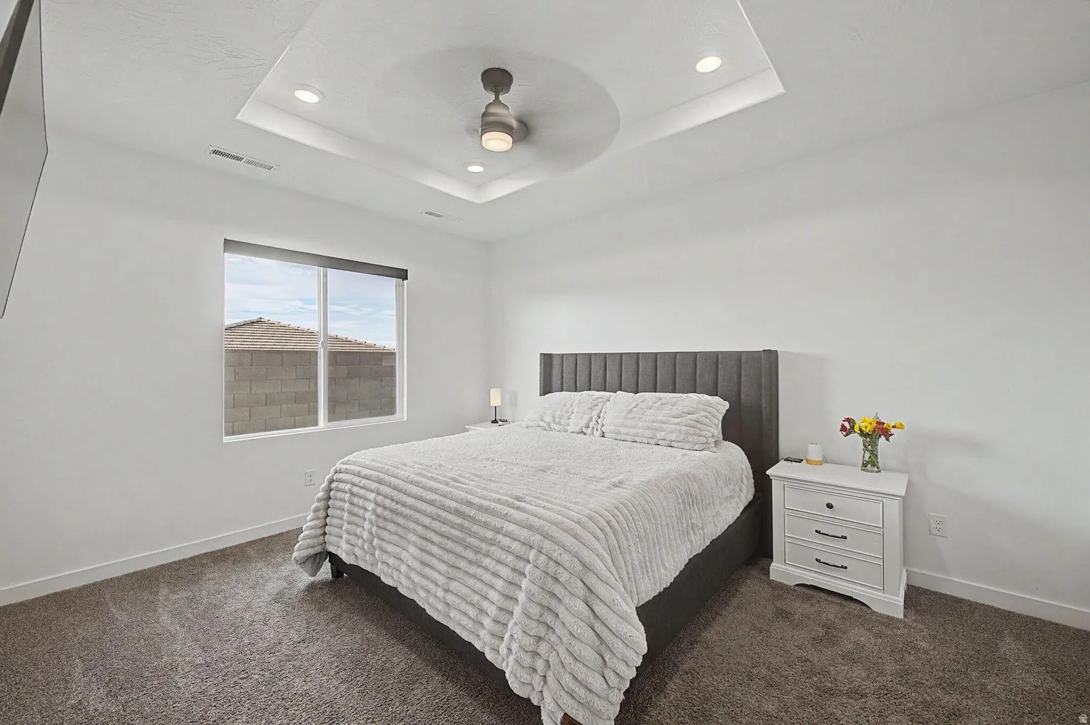Spacious bedroom featuring a tray ceiling with recessed lighting and a ceiling fan