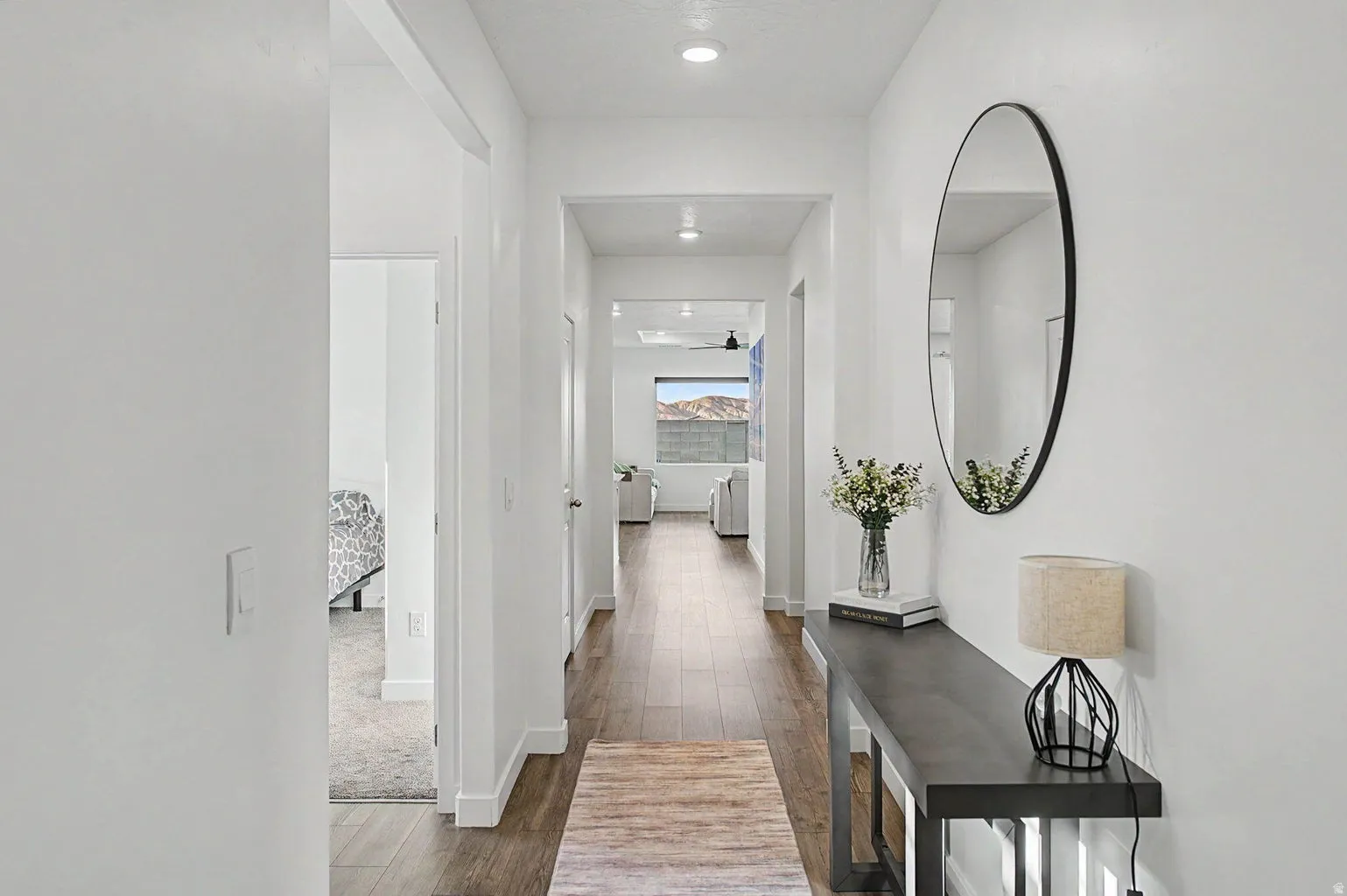 Bright hallway featuring wood-finish flooring, recessed lighting, white walls, and a visible mountain backdrop through a distant window
