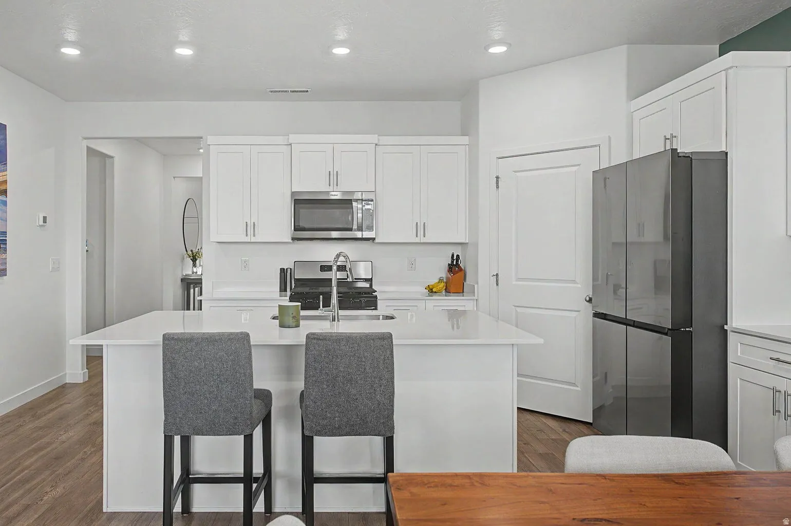Bright kitchen featuring a central island with countertop seating, white shaker cabinetry, stainless steel appliances, and wood-finish flooring