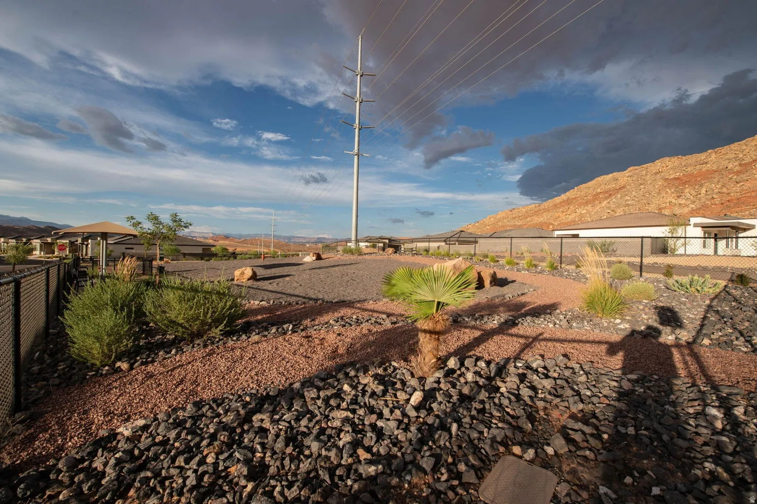 Landscaped property perimeter featuring a decorative rock path, low-maintenance desert plantings, and a black chain-link fence