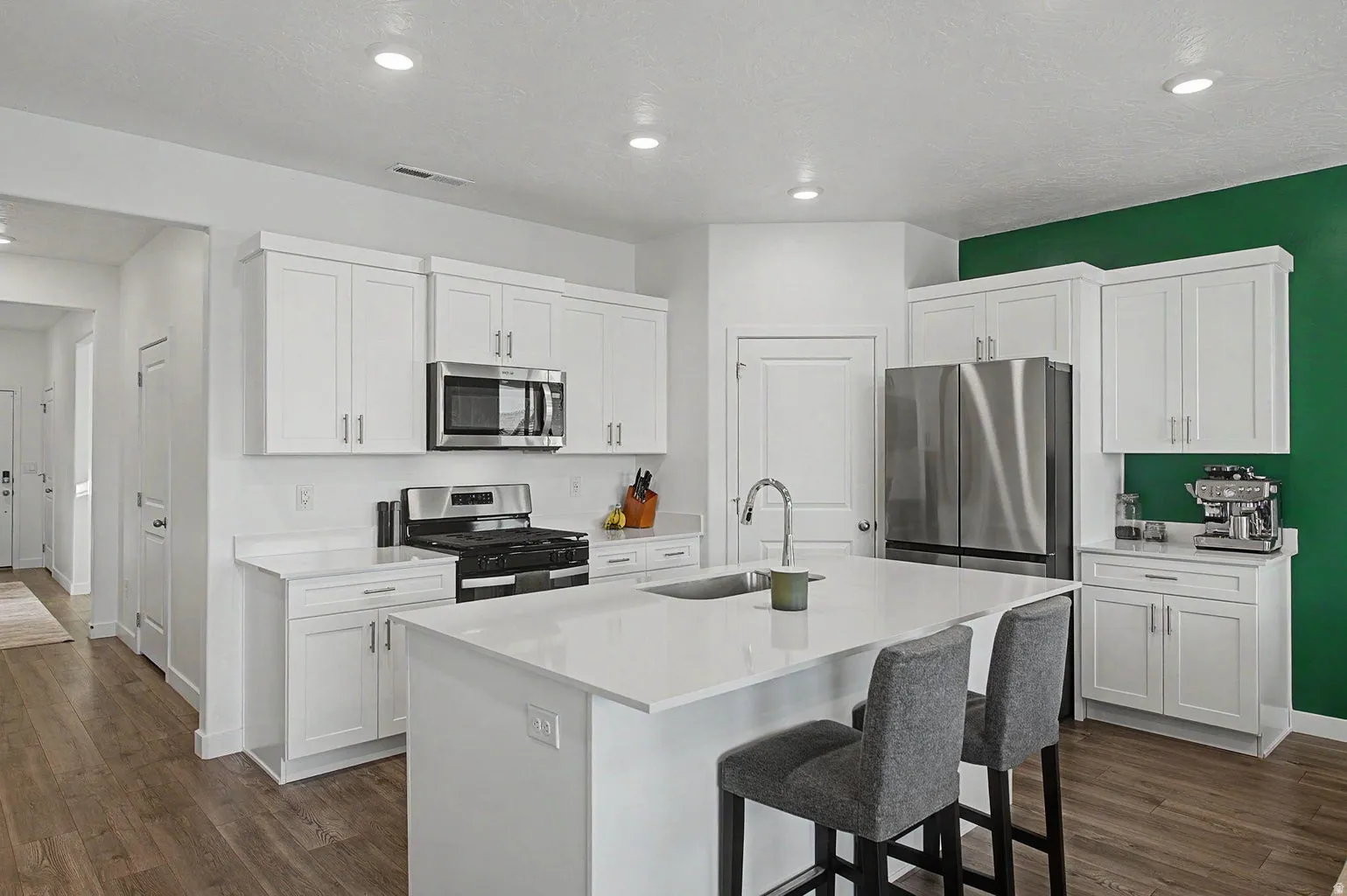 Modern kitchen featuring white shaker-style cabinetry, stainless steel appliances, a white countertop island with seating, recessed lighting, and wood-finish flooring