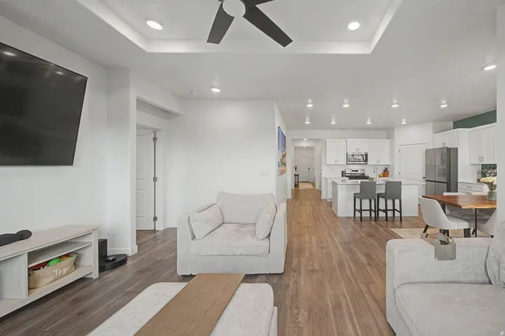 Open-concept living space featuring wood-finish flooring, recessed lighting, and a tray ceiling with a ceiling fan