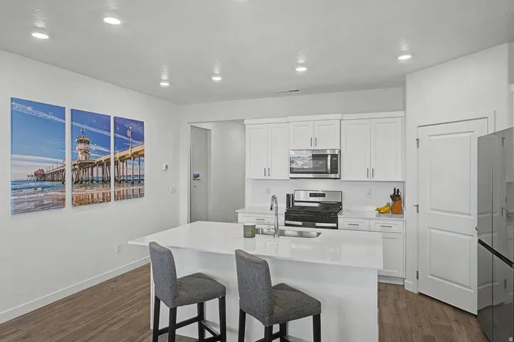 Modern kitchen featuring a white island with an undermount sink, stainless steel appliances, white cabinetry, and recessed lighting