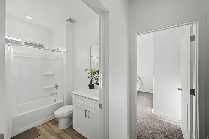 Bathroom featuring a white vanity with a white countertop and integrated sink, a white toilet, and a white tub and shower combination with a single-handle faucet