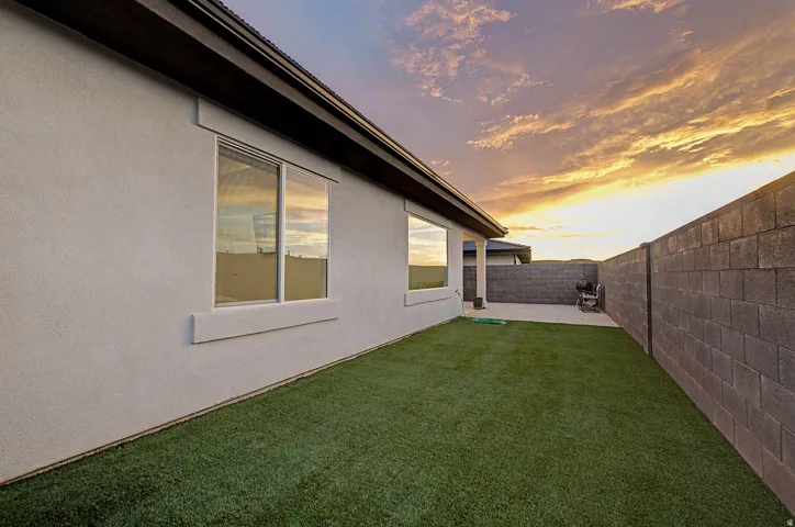 Private backyard featuring a stucco exterior, multiple windows with trim, a block wall perimeter, a paver patio, and artificial turf