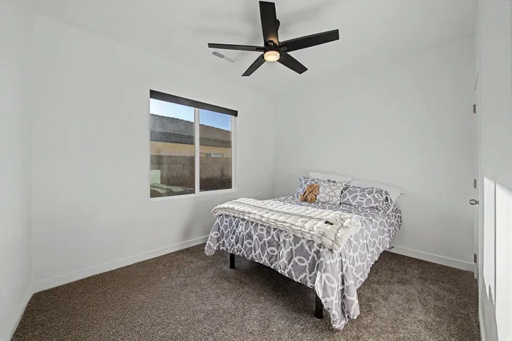 White walls with a ceiling-mounted fan, a window with a black roller shade, and plush carpet flooring