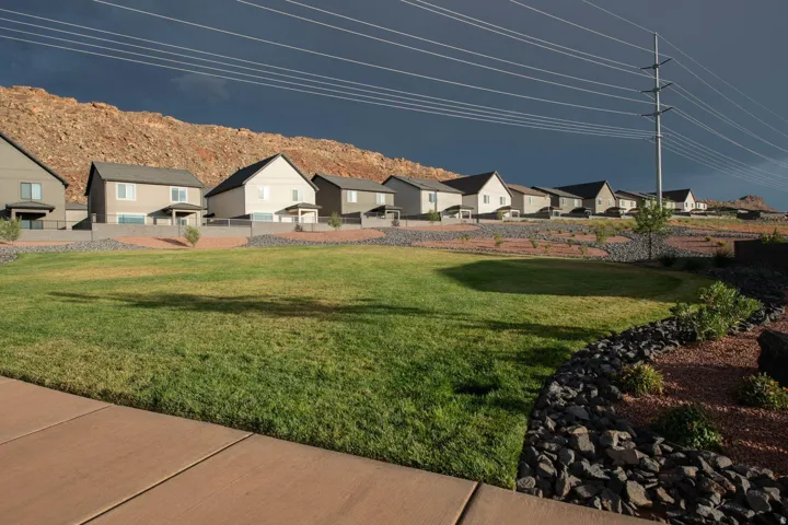 Expansive green space featuring a concrete walkway, rock landscaping, and a backdrop of rugged mountain terrain
