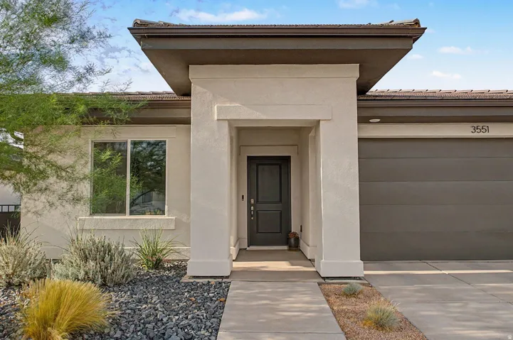 Contemporary stucco exterior featuring a prominent entryway with an overhang, a dark paneled front door, and an attached garage with a modern door