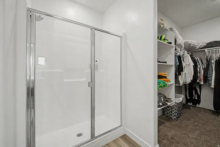 Walk-in shower with a glass enclosure and built-in shelving, complemented by wood-finish flooring