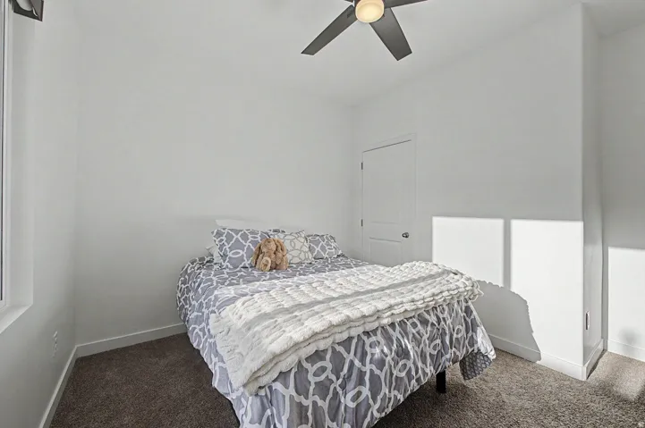 Bedroom featuring a window, ceiling fan, white walls, and dark carpet