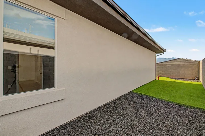 Stucco exterior with a modern window, dark roof fascia, and a rain gutter system