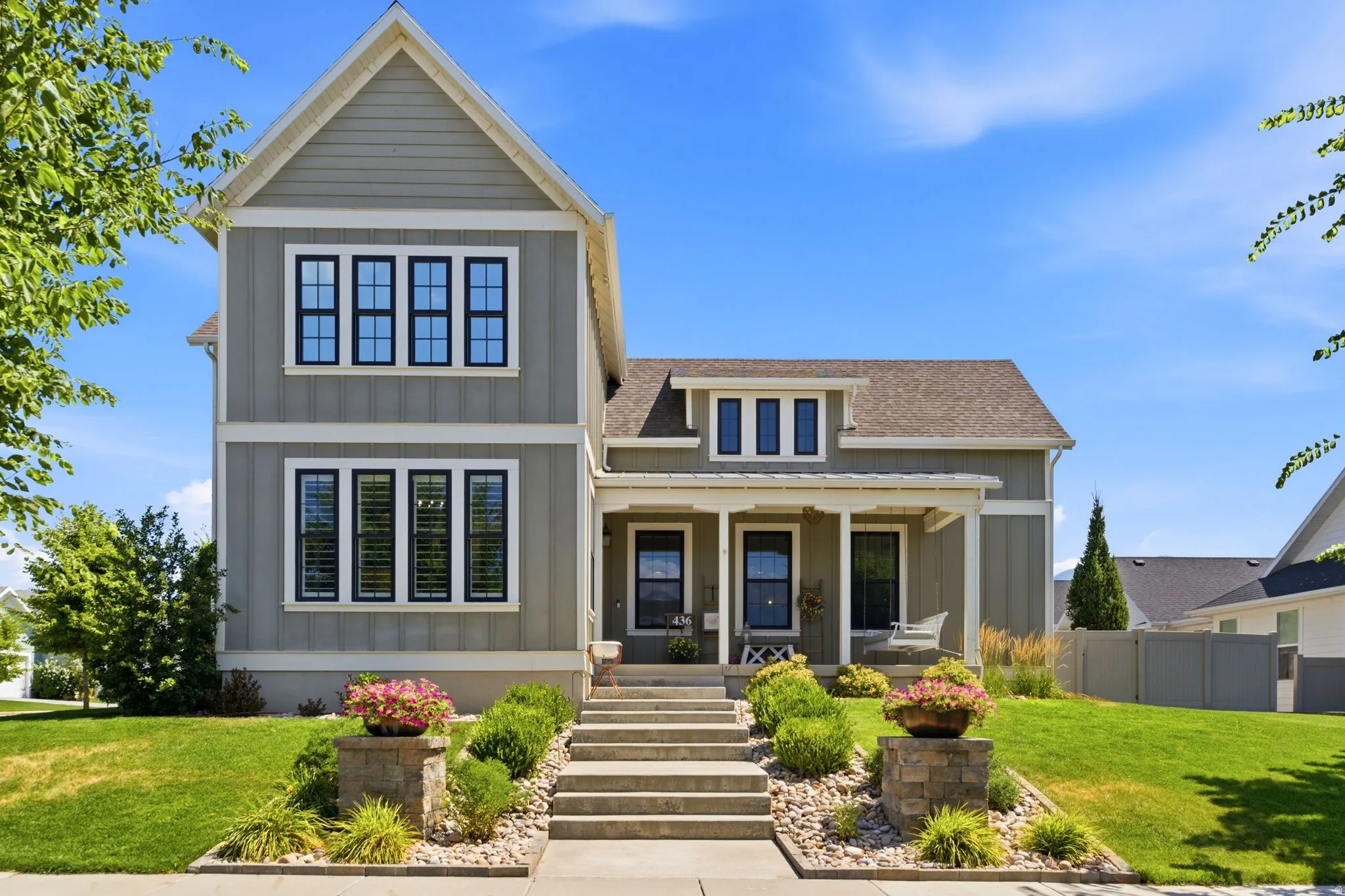 Modern farmhouse exterior featuring vertical and horizontal siding, a covered porch,  gabled roof and  stone-edged landscaping