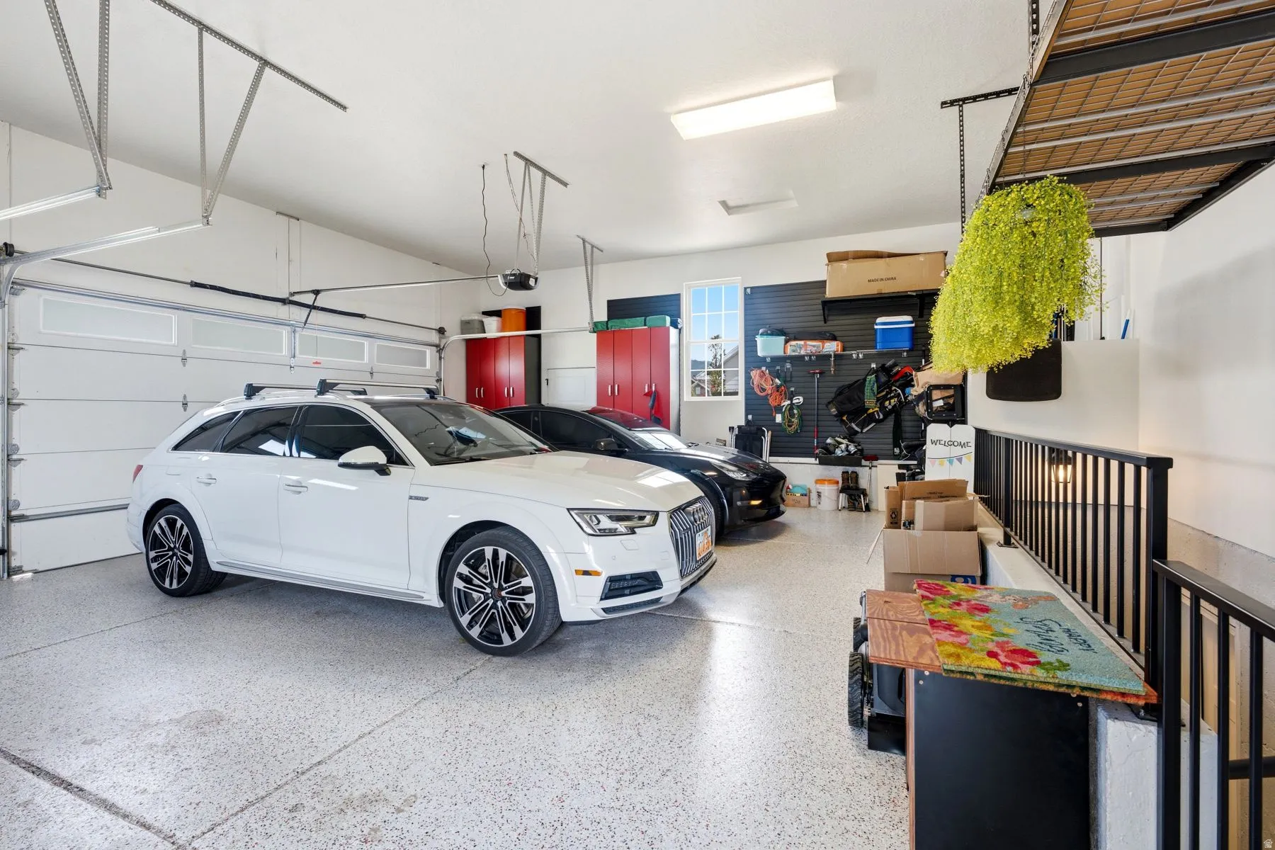 Three-car garage featuring epoxy-coated concrete floor, custom overhead storage racks and wall racks-Stairs to ADU