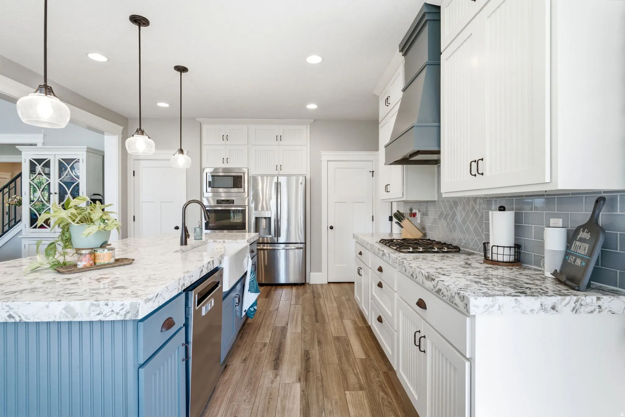 Gourmet kitchen featuring a spacious island with a farmhouse sink, stainless steel appliances, wood-finish flooring, and subway tile backsplash