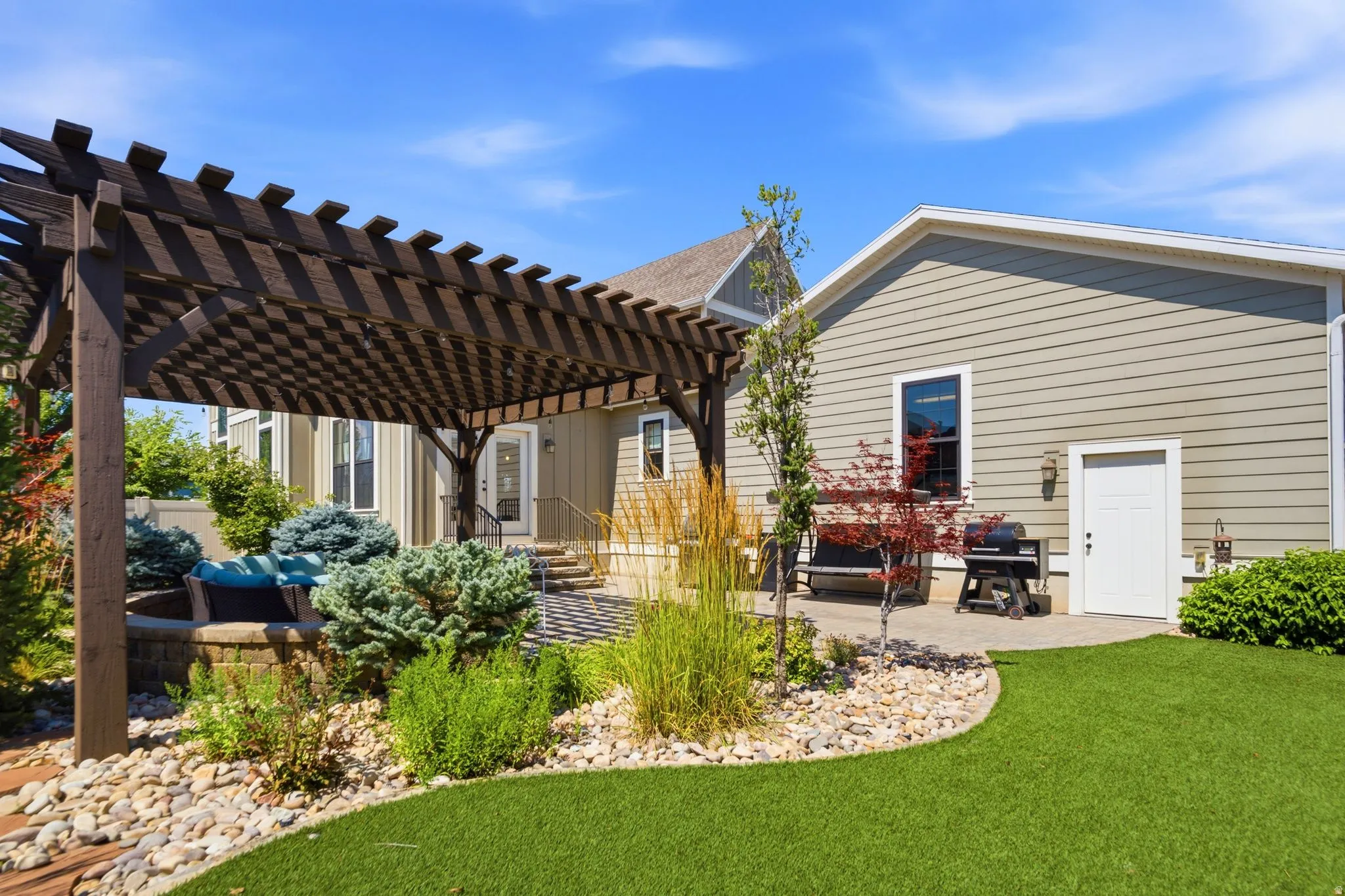Expansive backyard featuring a dark wood pergola, artificial turf showing man-door to the garage