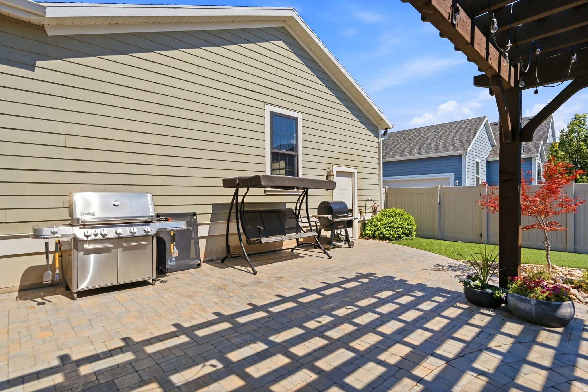 Paver patio extends from the property exterior, featuring a wood pergola and artificial turf lawn area