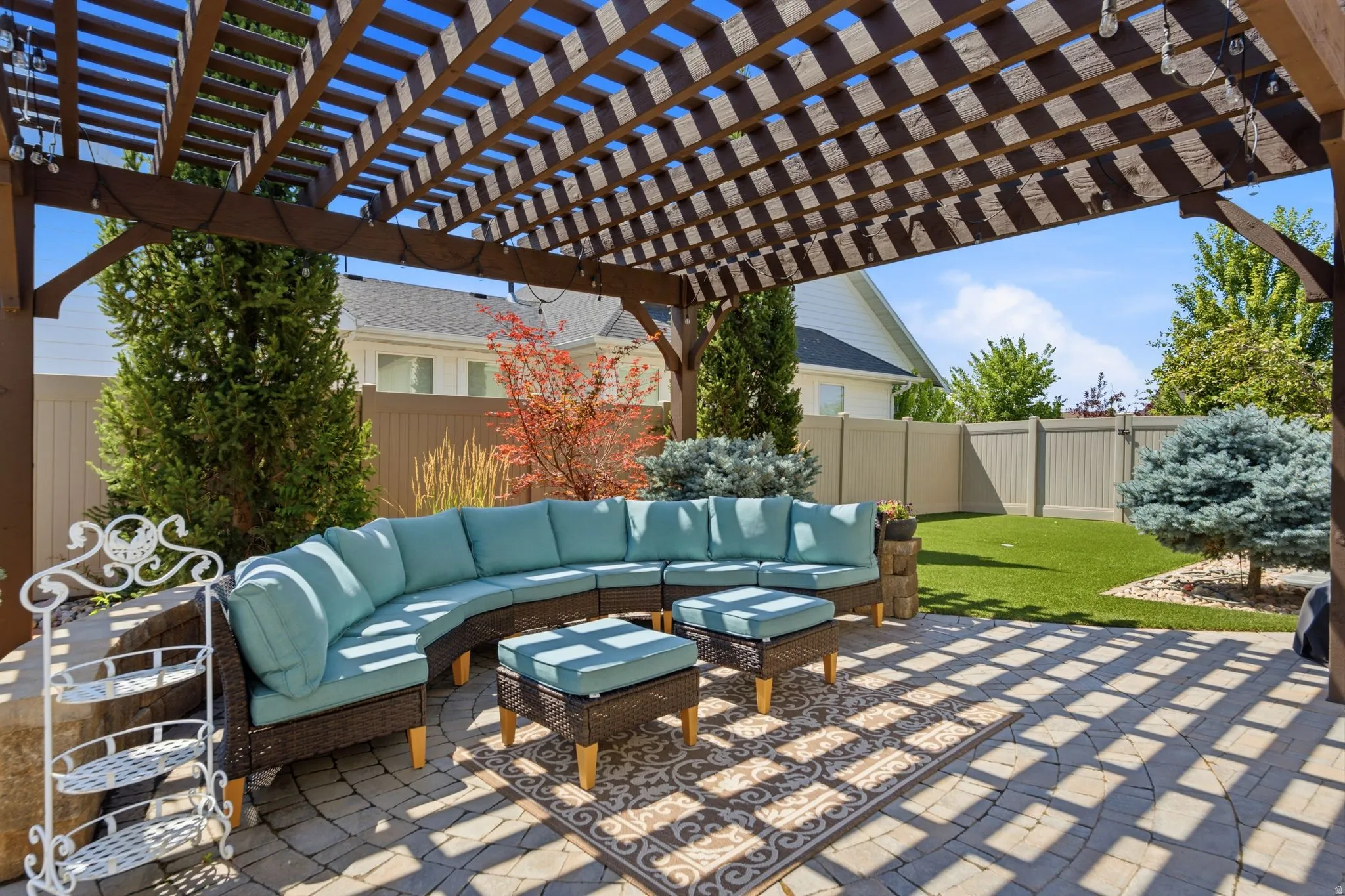 Expansive paver patio featuring a large wooden pergola, artificial turf, and mature landscaping