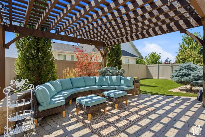 Expansive paver patio featuring a large wooden pergola, artificial turf, and mature landscaping