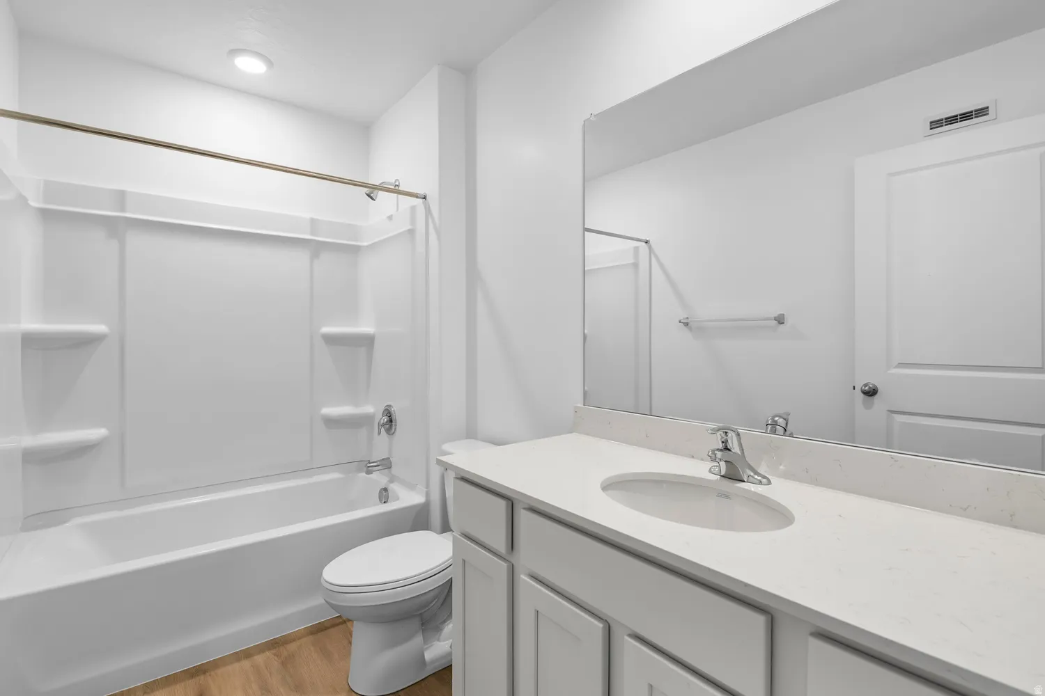 Bathroom featuring a white vanity with an undermount sink, a large wall-mounted mirror, a tub/shower combination with a white surround, and wood-finish flooring