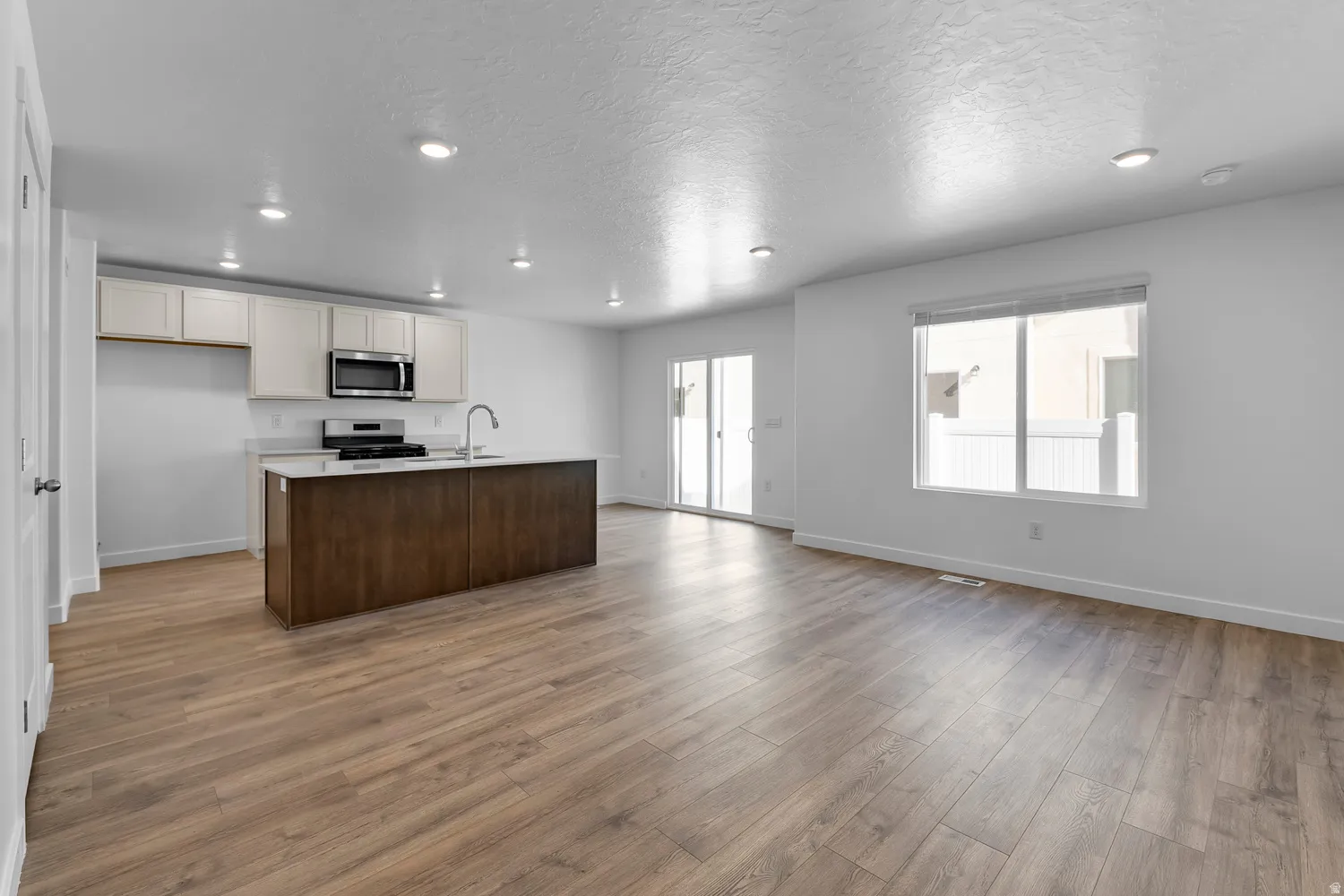 Open-concept living space with wood-finish flooring, a kitchen island, white cabinetry, recessed lighting, and a sliding glass door