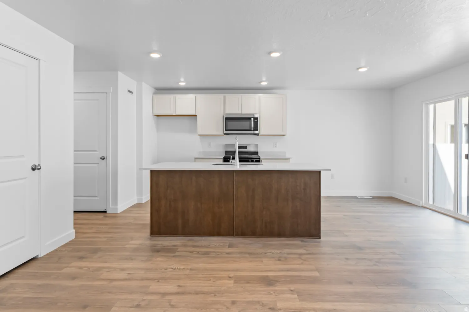 Open-concept kitchen featuring a central island with a wood-finish base, light-toned countertops, stainless steel microwave, and white cabinetry