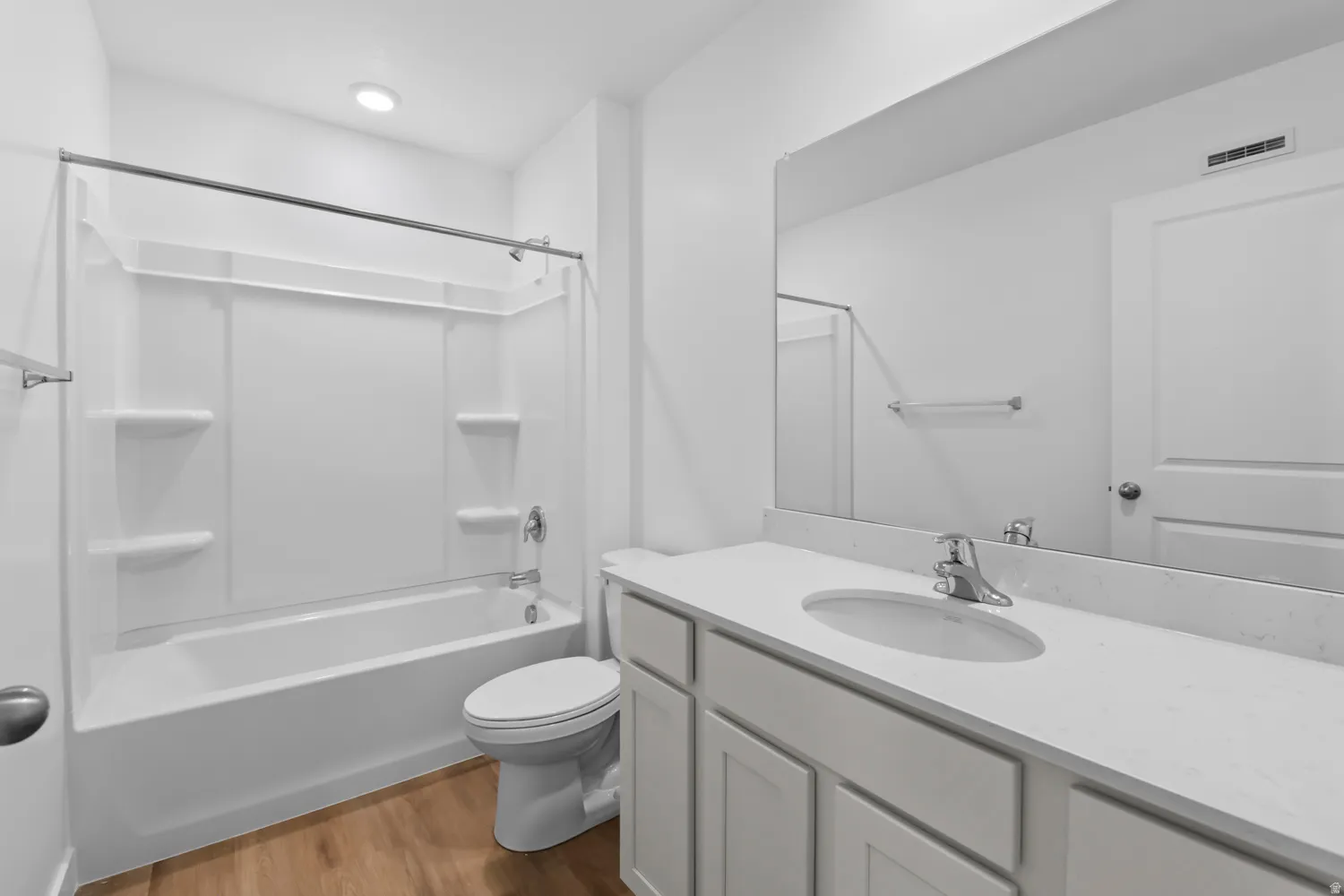 Bathroom featuring a white bathtub with an integrated shower, a single vanity with a white countertop, and wood-finish flooring