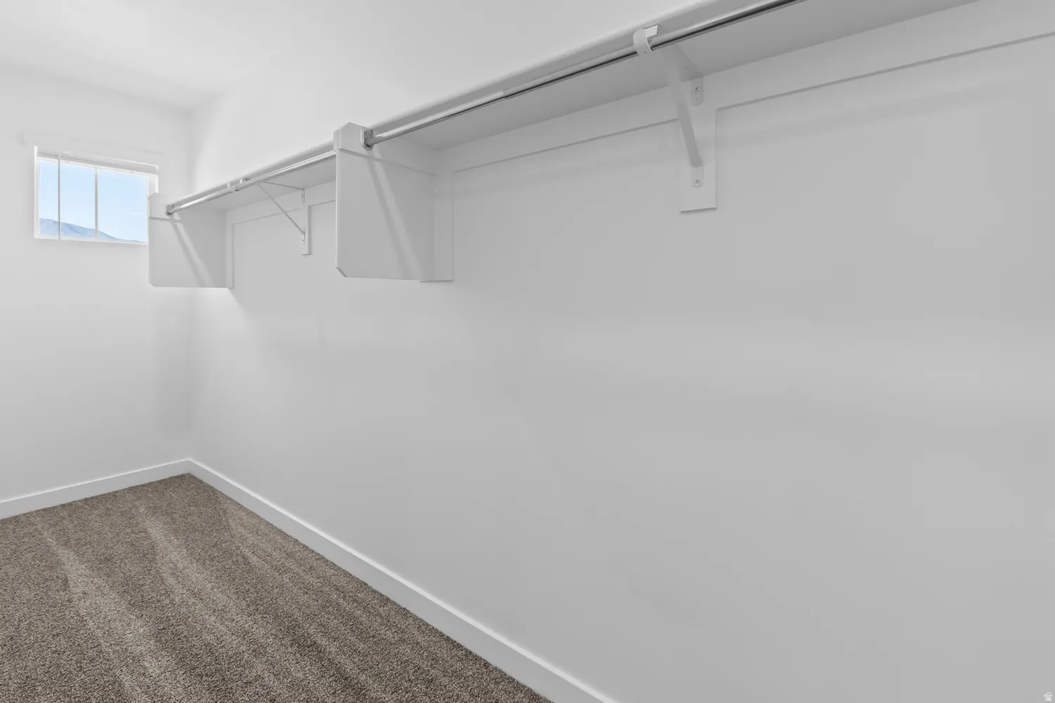 Interior closet space featuring a single window, white walls, white baseboards, and gray patterned carpet